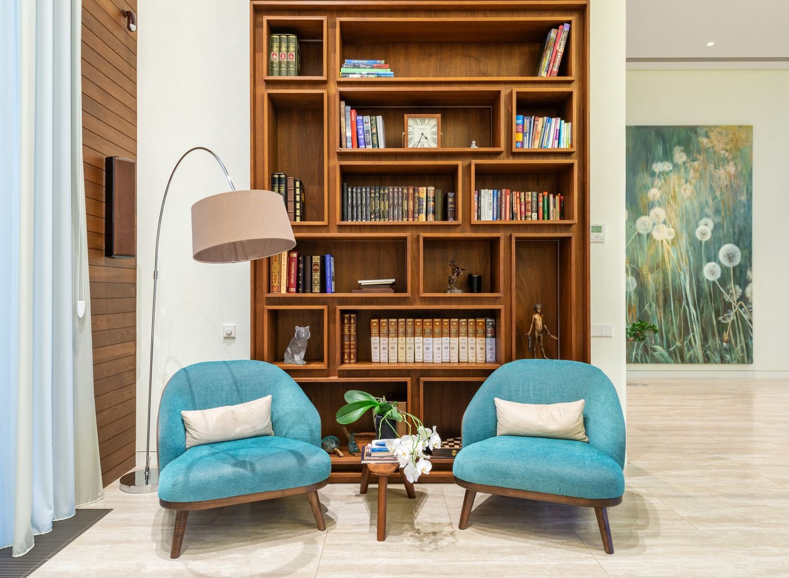 Warm living room corner with a built-in wood bookcase, arc floor lamp and two curved armchairs