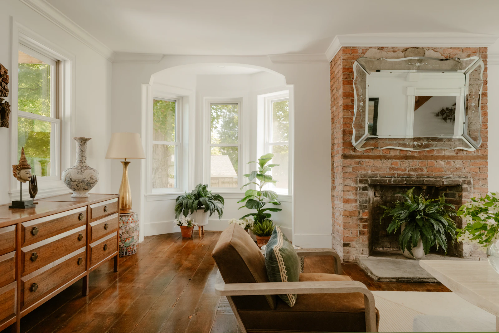 Elegant living room with a brick fireplace, vintage mirror, wood dresser and potted ferns