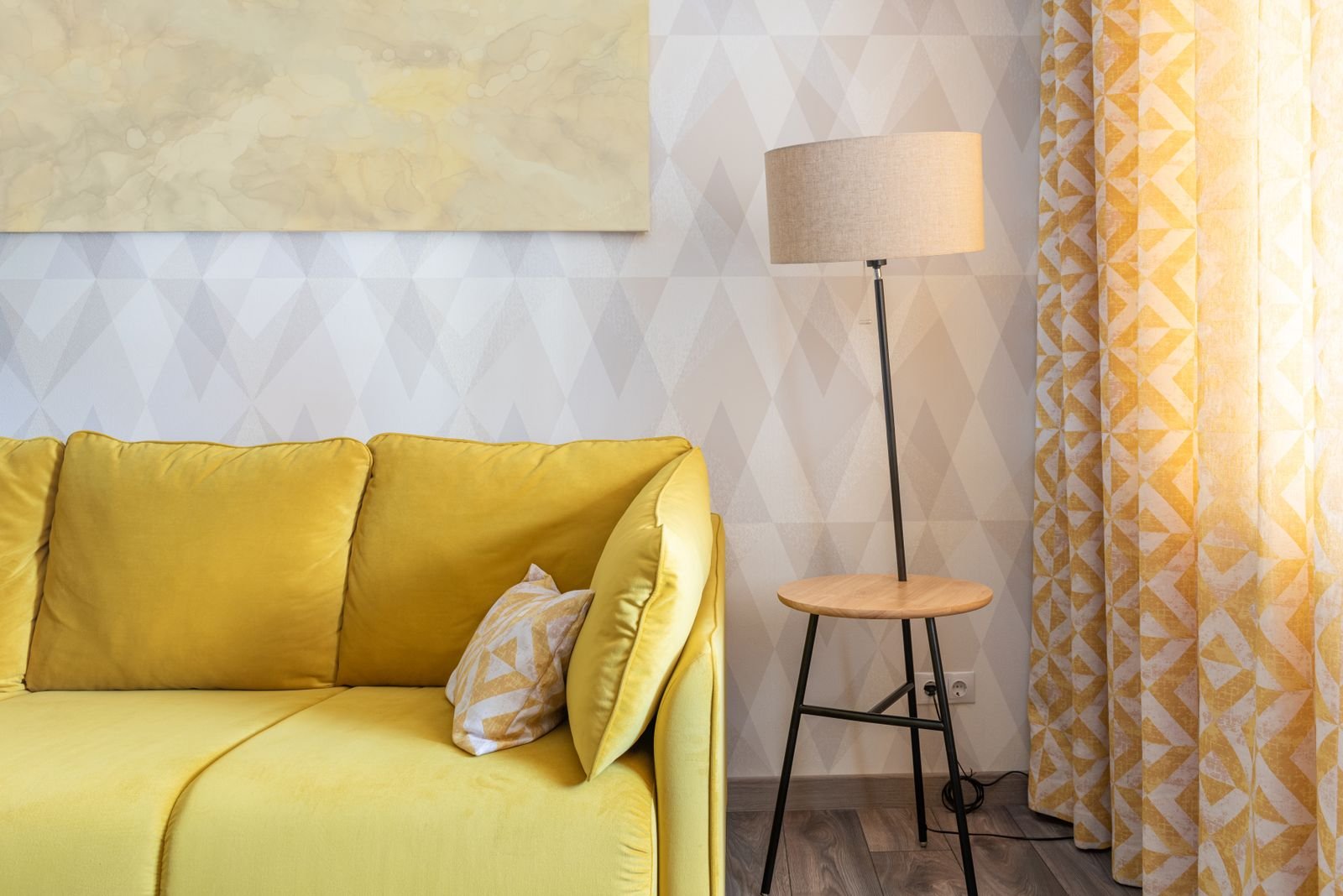 Living room corner with a warm linen-shade floor lamp glowing beside a yellow sofa and patterned curtains
