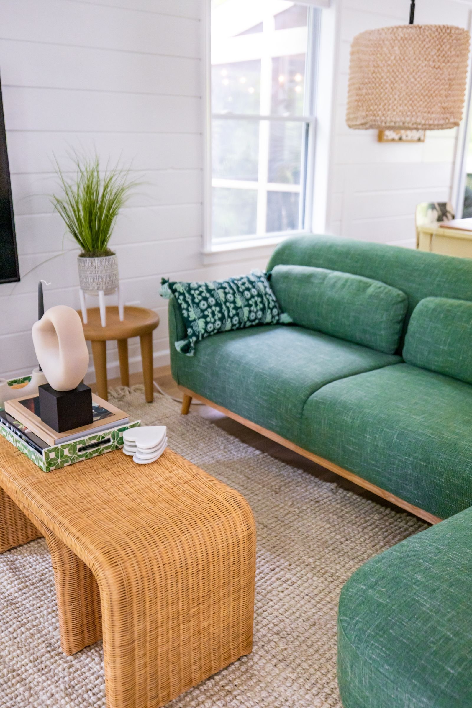 Living room with a sage green sofa, woven rattan coffee table and a natural pendant light