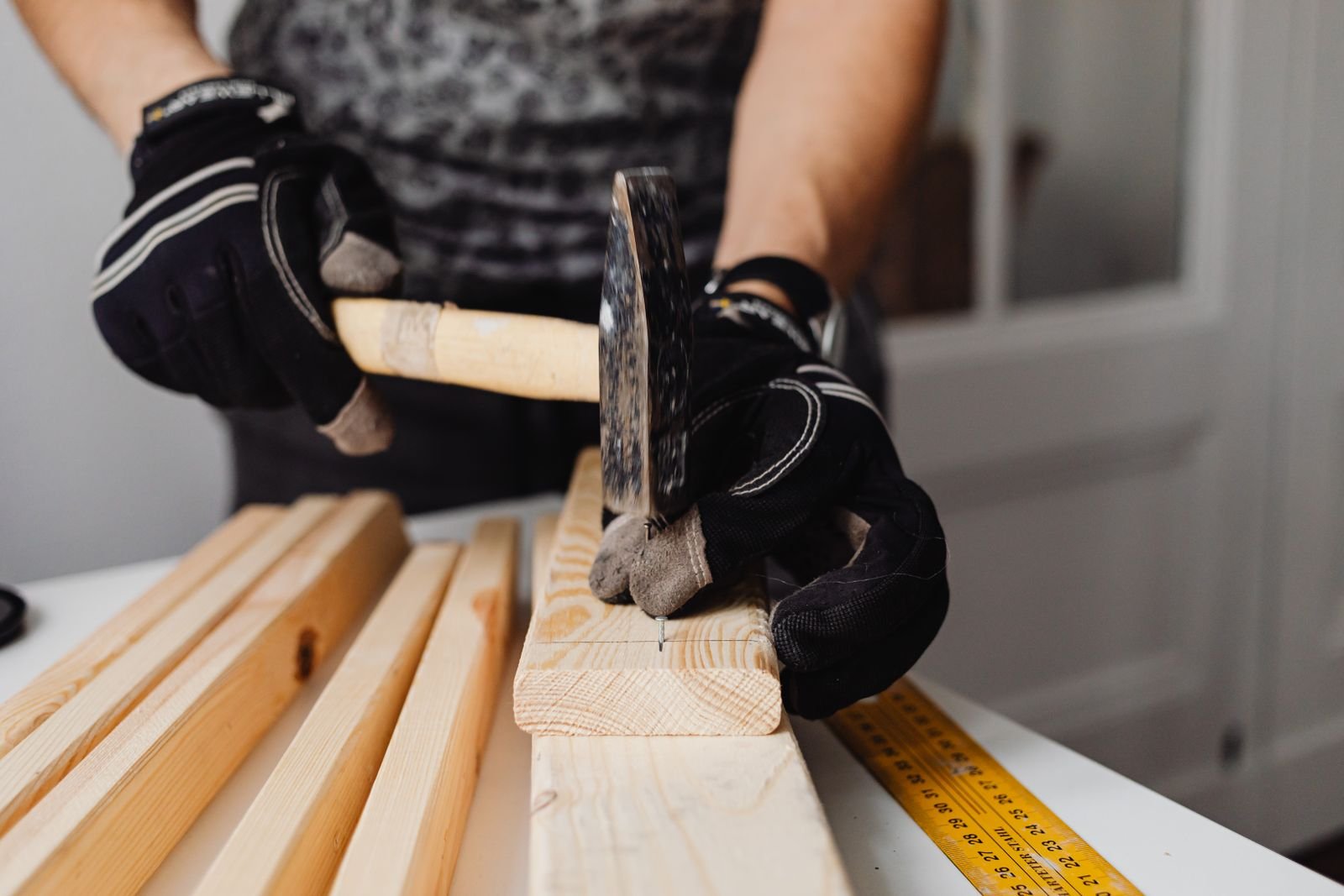 Close-up of gloved hands hammering a nail into a wood board during a home improvement project