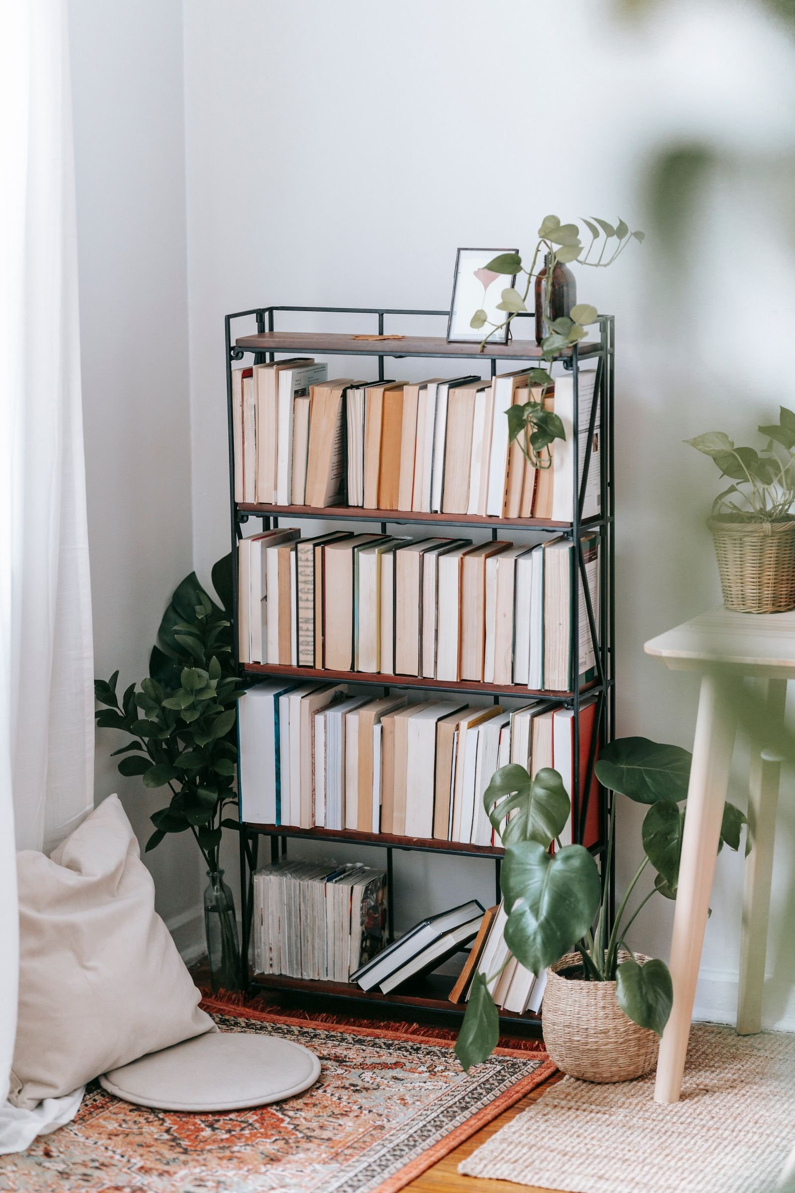 Small apartment corner with a patterned rug defining the space and a tall narrow bookshelf against the wall