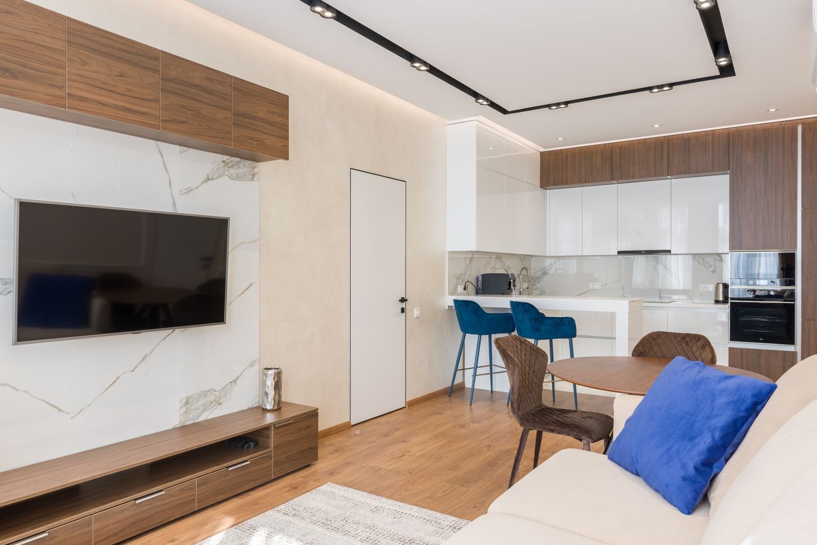 Open-plan living space with a sofa and TV console in one zone and a round dining table in another, each defined by its own rug