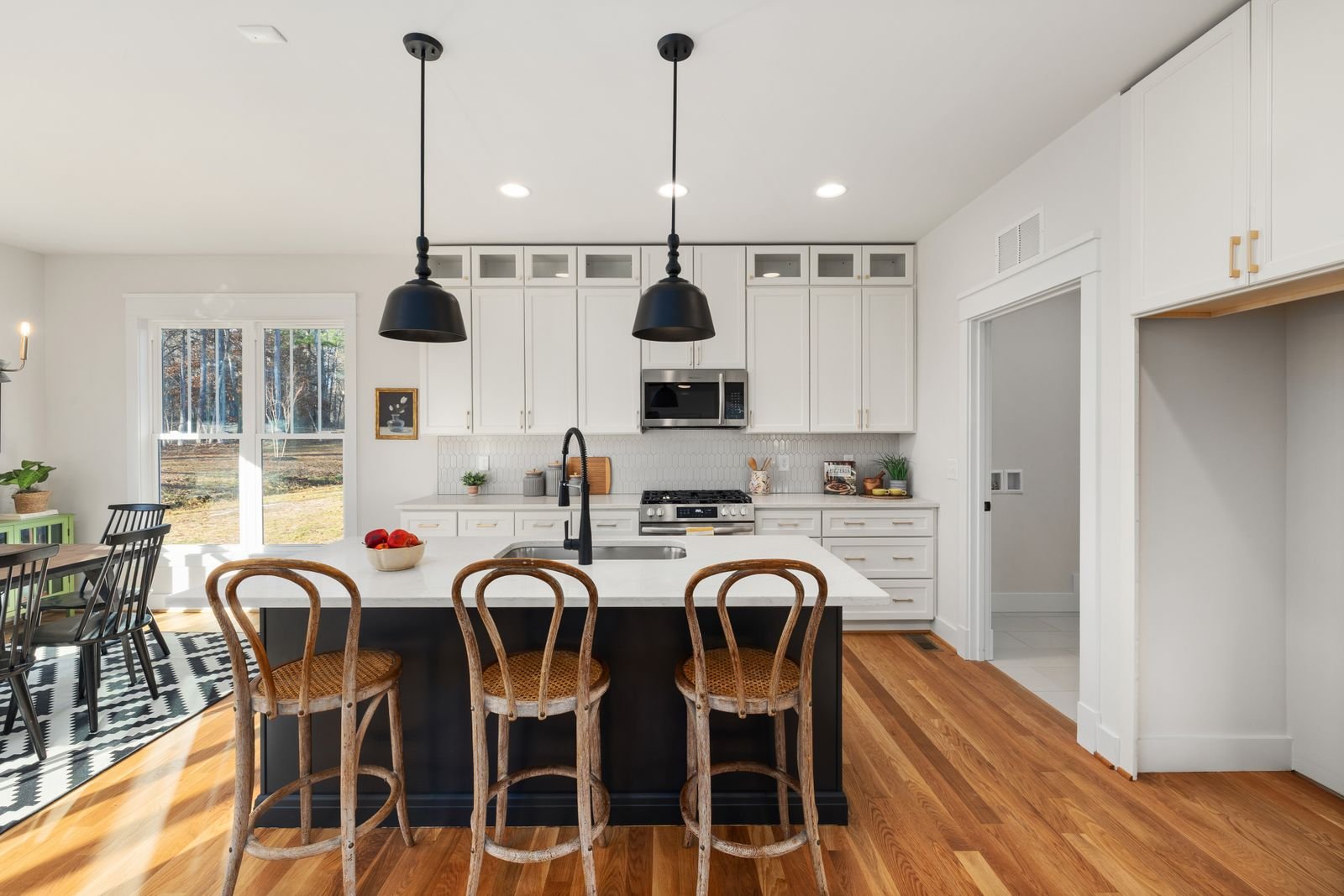 Modern farmhouse kitchen with white cabinets, black pendant lights and fixtures, and a wood-topped island with rattan stools