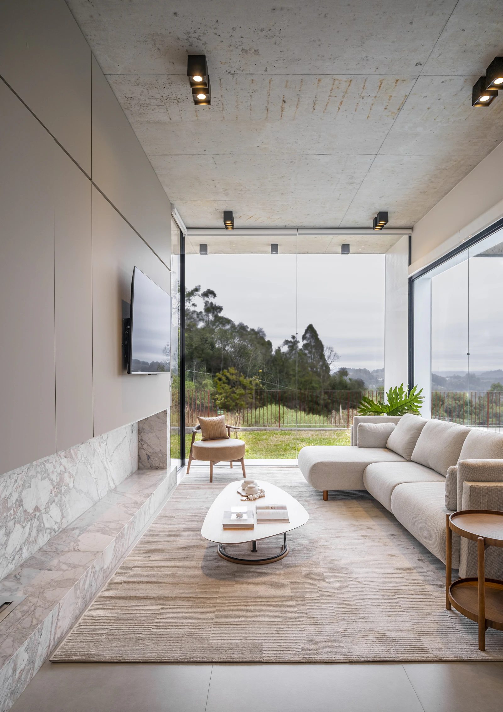 Bright modern living room with an L-shaped sofa, oval coffee table and floor-to-ceiling windows overlooking greenery