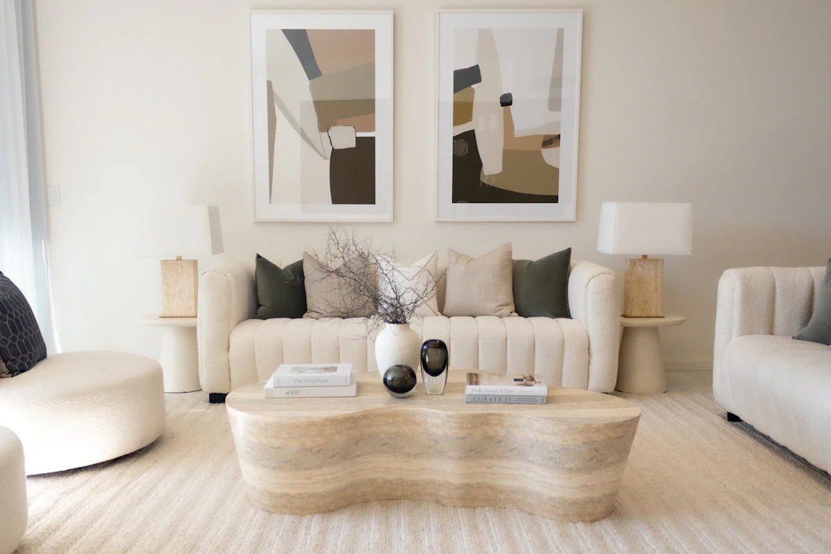 Neutral-toned living room with cream boucle sofas, tan stone side tables and a curved travertine coffee table