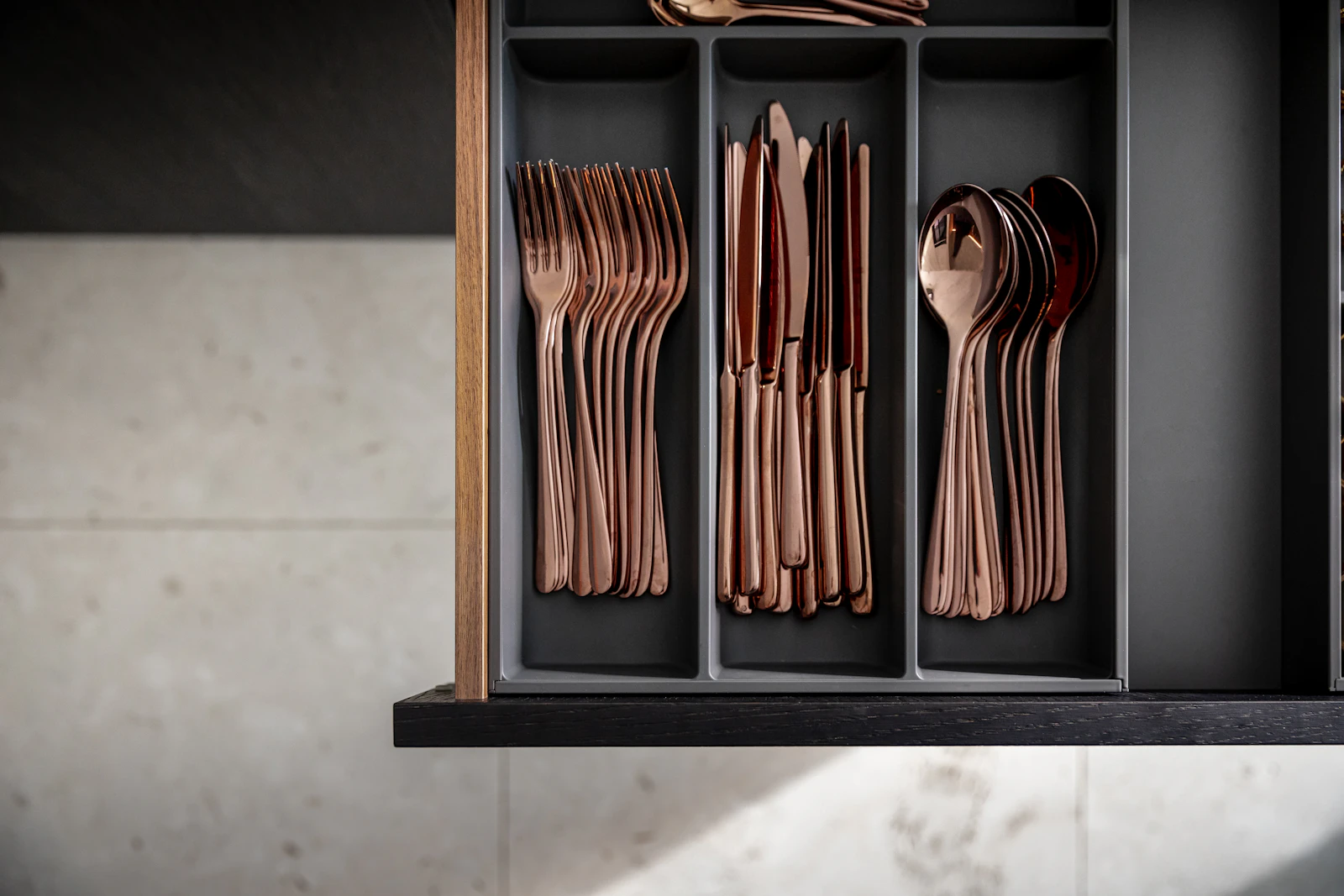 Organized kitchen drawer with dividers separating rose-gold forks, knives and spoons by type