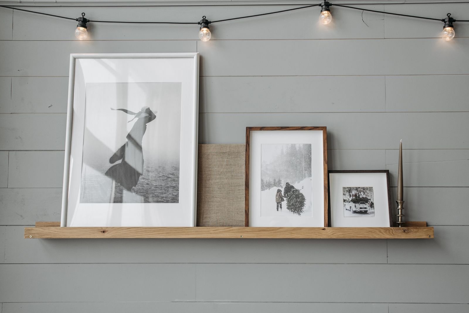 Narrow wood picture ledge holding a mix of leaning black-and-white framed prints against a shiplap wall