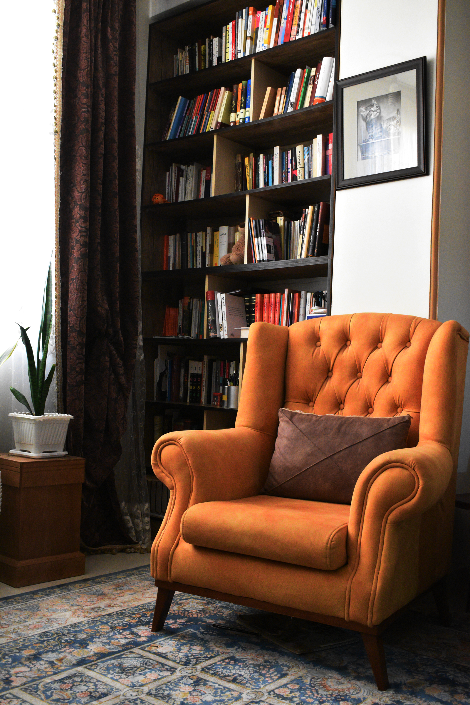 Living room reading corner with a tufted orange armchair, a full bookshelf and a patterned rug underfoot