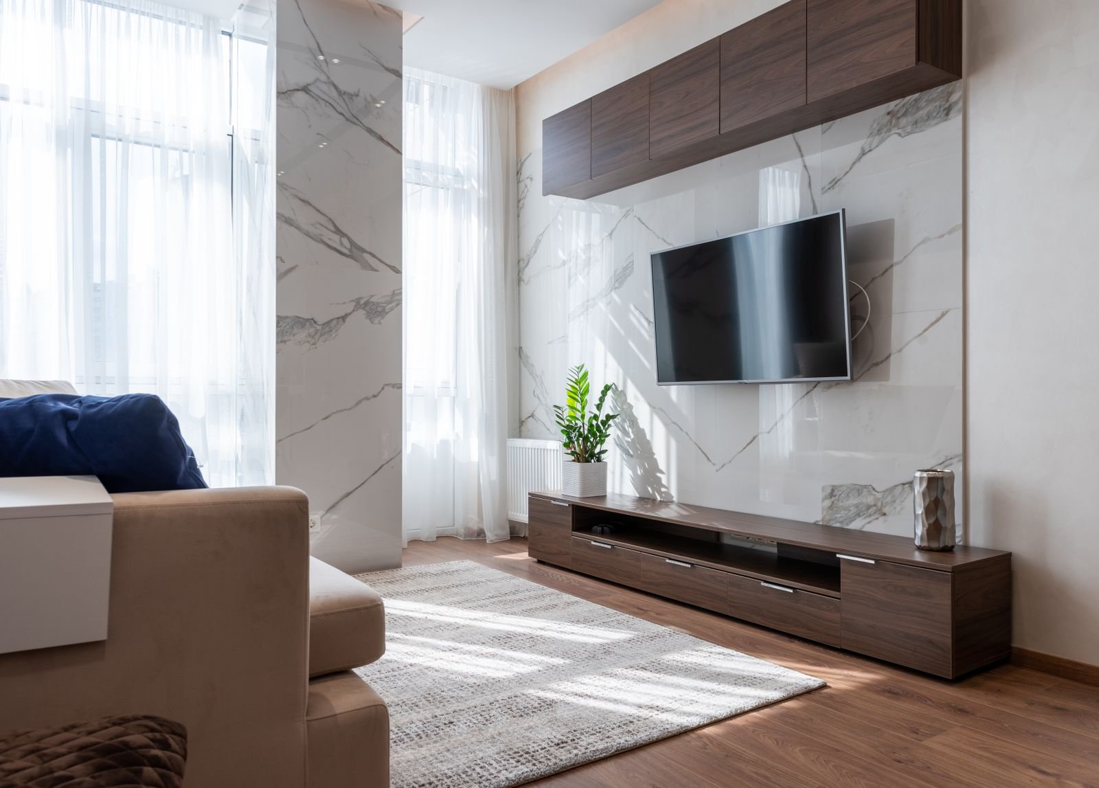 Living room styled with warm walnut cabinetry, a marble accent wall and sheer curtains